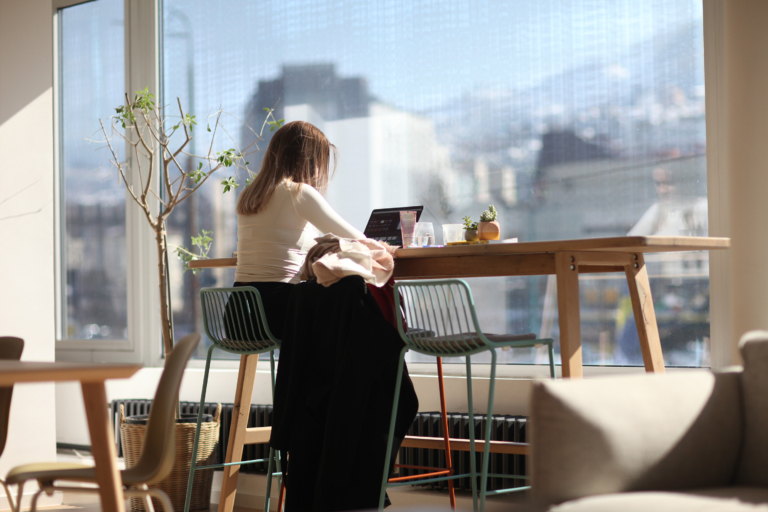 Professional working in coworking space in Sarajevo, seated on bar stool at standing desk near panoramic windows with a view of Sarajevo