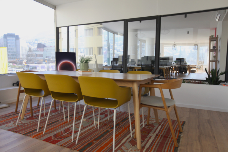 Modern and aesthetic conference room in a coworking space in Sarajevo, with a wood desk, designer chairs, ethnic rug and flip TV.