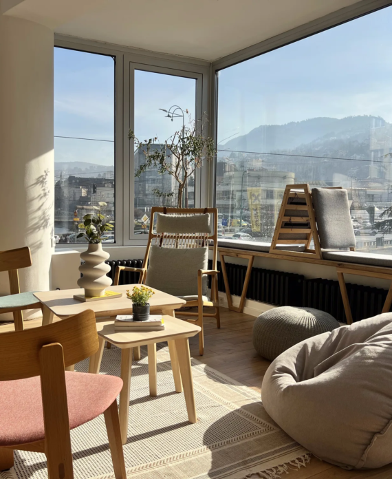 Cozy lounge corner in Motiff coworking space with wooden chairs, pink accent chair, and beanbag seating overlooking Sarajevo's mountains