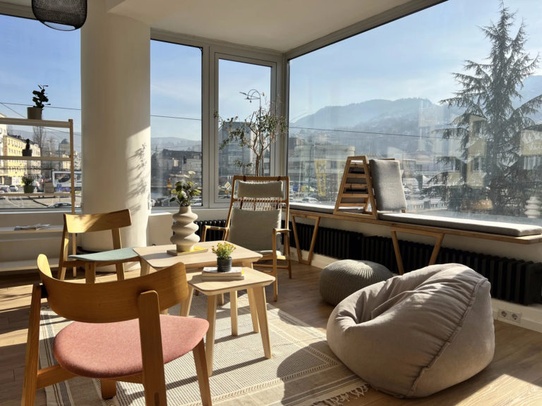 Cozy lounge corner in Motiff coworking space with wooden chairs, pink accent chair, and beanbag seating overlooking Sarajevo's mountains