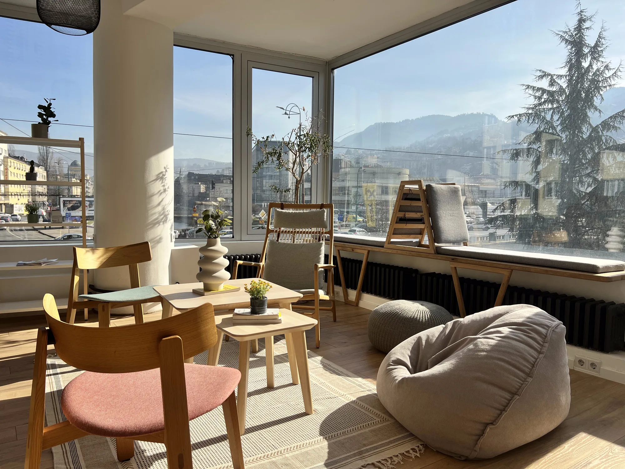 Cozy lounge corner in Motiff coworking space with wooden chairs, pink accent chair, and beanbag seating overlooking Sarajevo's mountains