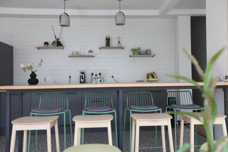Kuhinja i coffee bar sa pločicama, otvorenim policama i barskim stolicama u Motiff coworking prostoru u Sarajevu