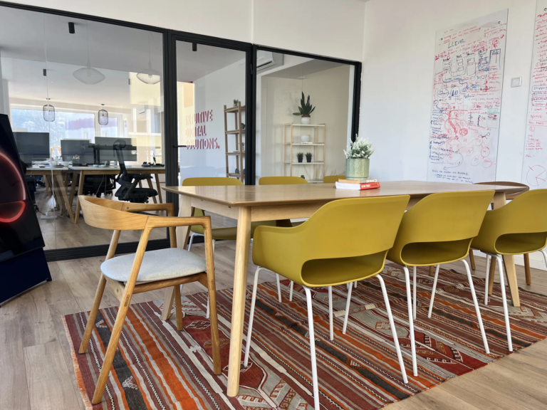 Meeting table with mustard chairs on a traditional rug, whiteboard in the background at Motiff coworking space in Sarajevo