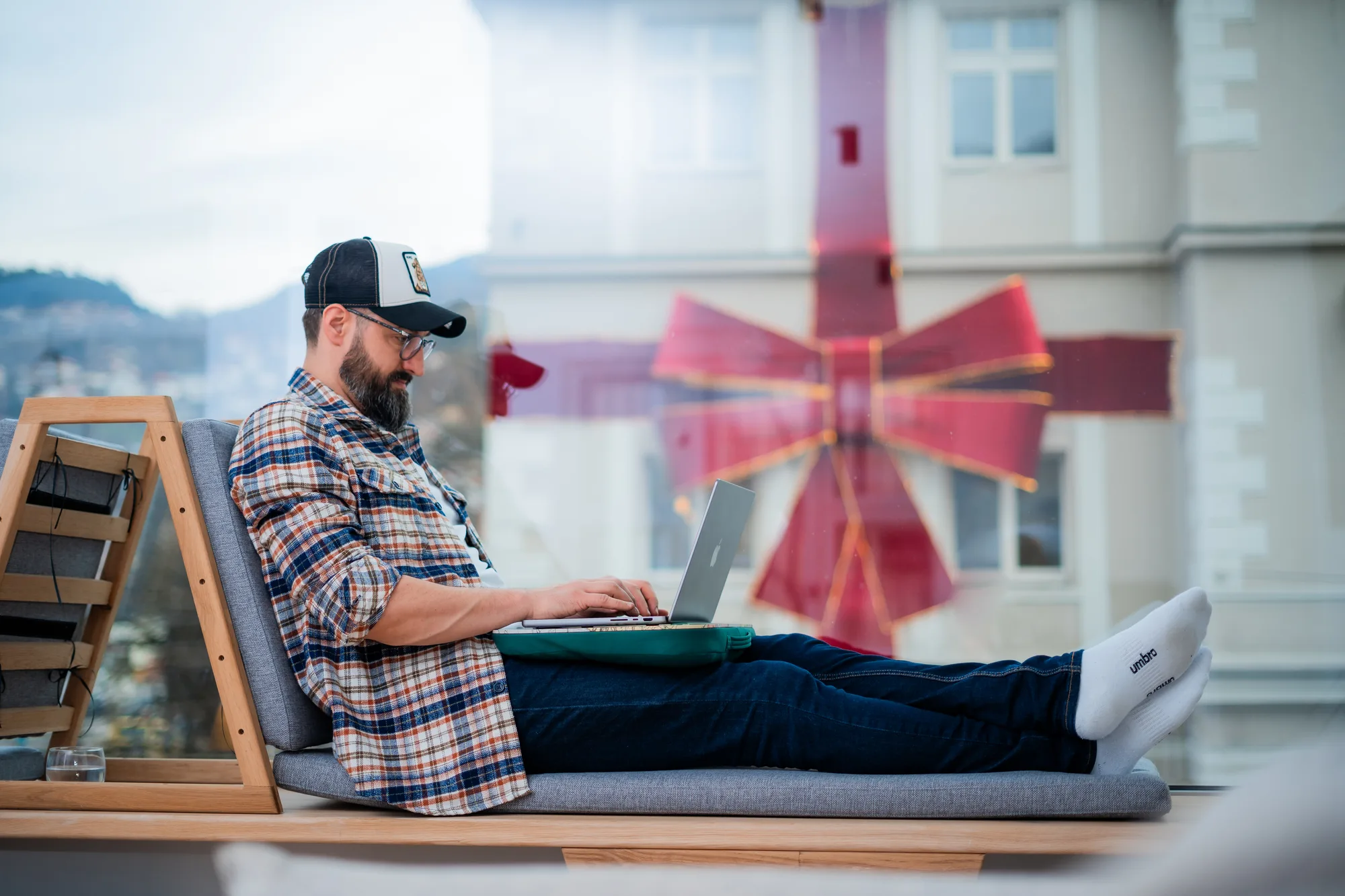 Frilenser opušteno radi na laptopu na klupi pored prozora u Motiff coworking prostoru u Sarajevu